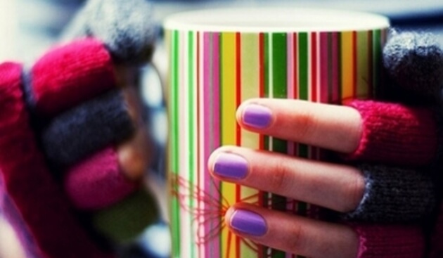 Mani fredde con guanti e tazza colorata