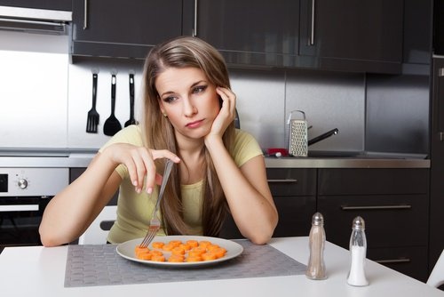 ragazza triste davanti a piatto di carote