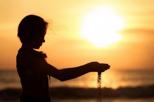 bambina con sabbia tra le mani al tramonto