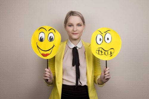 Donna che tiene cartelli con facce che mostrano emozioni opposte, rappresentando la sua capacità di gestire le emozioni