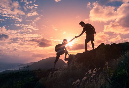 Un ragazzo che aiuta una ragazza in montagna, aiutandola a creare la resilienza