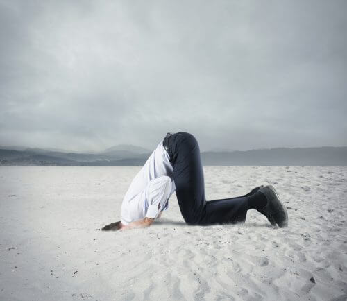 Uomo che ha paura e nasconde la testa sotto alla sabbia