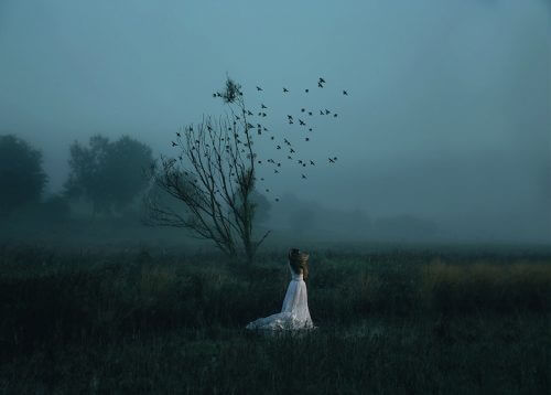 Donna davanti ad un albero spoglio con degli uccelli che volano