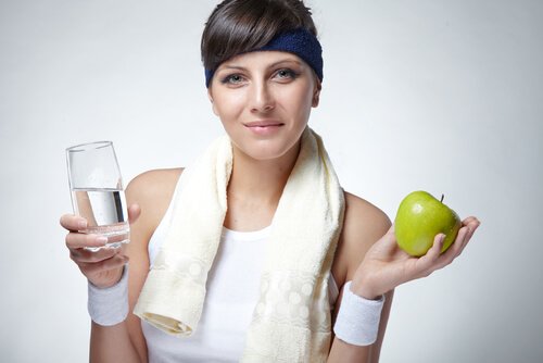 Donna che tiene in mano un bicchiere di acqua e una mela abitudini mattutine