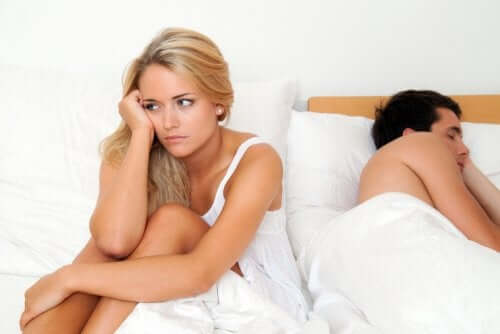 Donna che pensa seduta sul letto mentre il partner dorme
