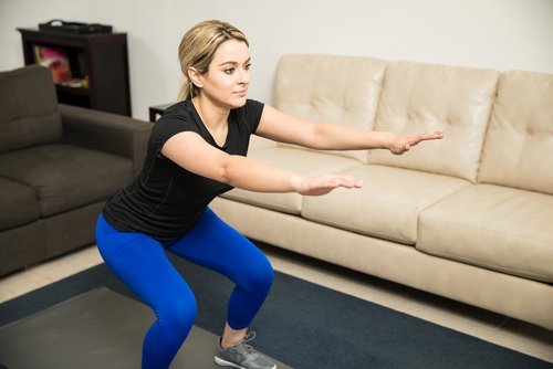 Esercizi di squat eseguiti da donna in salotto