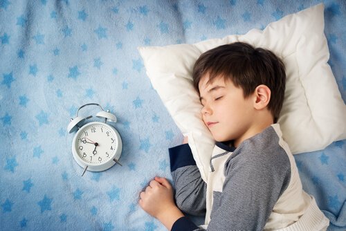 Niño durmiendo sereno con reloj despertador al lado