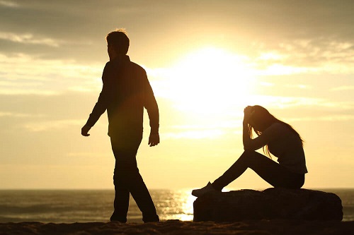 donna seduta su scoglio al mare e uomo che si allontana