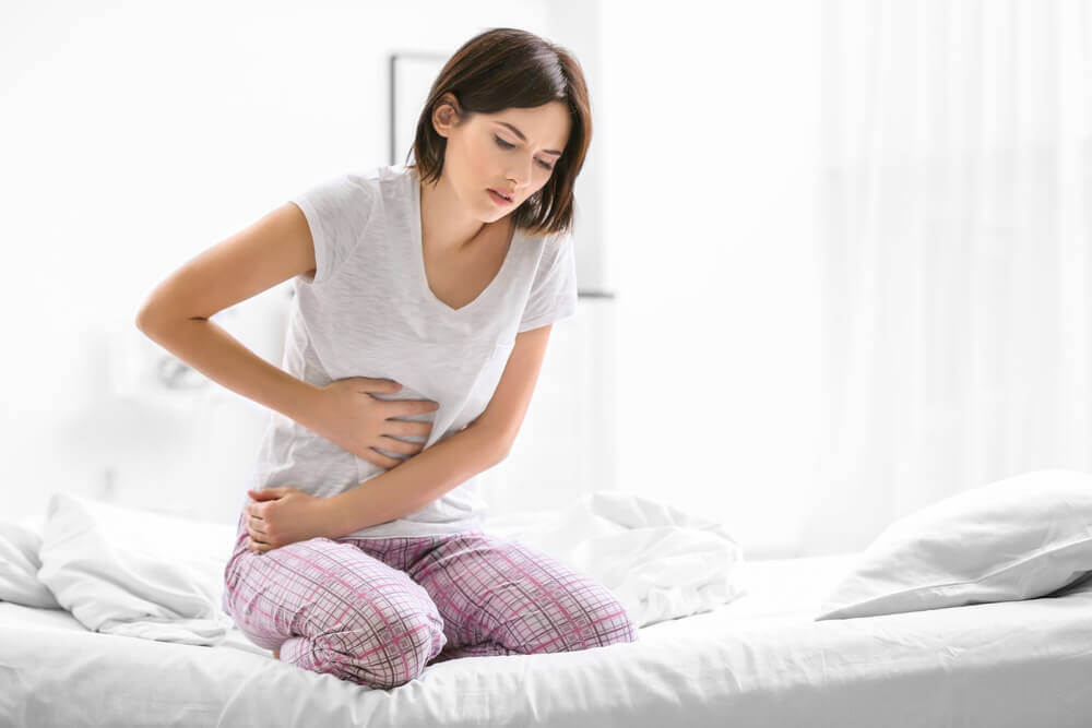 Infezione da Helicobacter pylori: donna sul letto in pigiama con dolore allo stomaco.