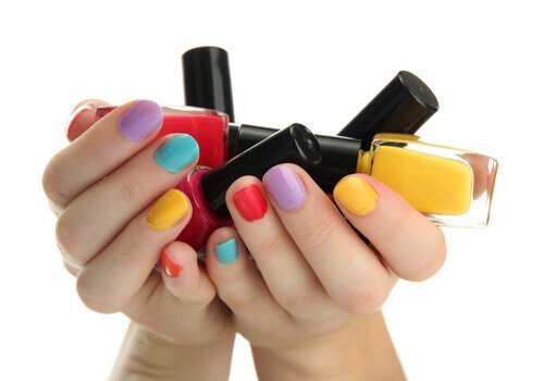 Mani con un colore diverso per ogni unghia e boccette di smalto