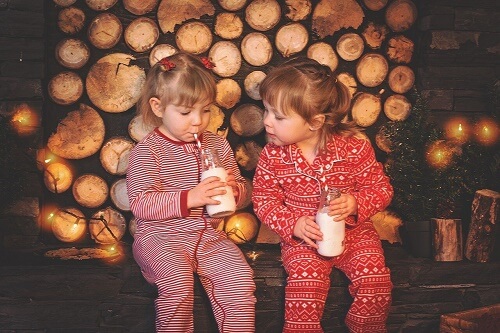 Due bimbe piccole bevono latte sedute davanti alla legna