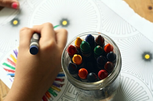 Mano di bambino che disegna accanto a portapenne con pastelli colorati