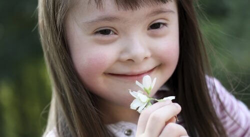 Bambina down tiene fiorellino in mano davanti alla bocca.