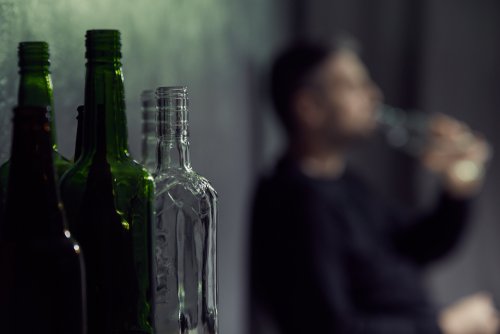 Bottiglie di vetro e in fondo uomo beve alchol