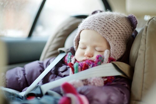 Neonata con cappello e giubbotto dorme in seggiolino auto