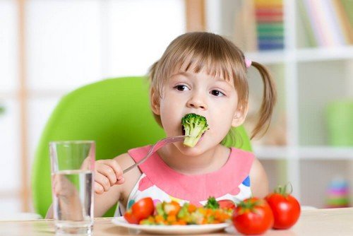 bambina seduta a tavola mangia i broccoli