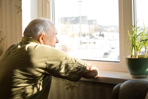 Uomo anziano guarda attraverso finestra chiusa