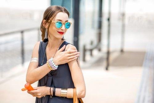 Donna che cammina per la città spalmandosi crema solare
