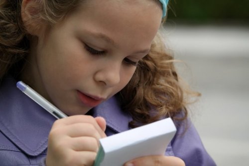 Bambina che scrive su di un block notes esercizi di ortografia