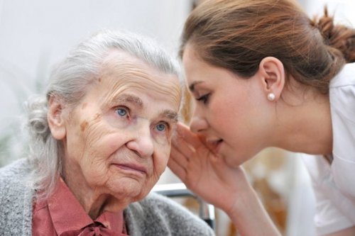 Donna giovane parla all'orecchio di una donna anziana