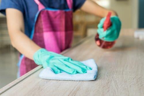 Donna pulisce una superficie di legno con panno e detergente