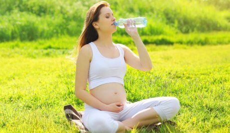 Donna incinta che beve acqua seduta sul prato.