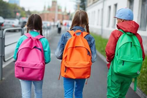 Tre ragazzi vanno a scuola indossando abiti e zaini colorati.