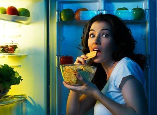 Ragazza davanti al frigo che mangia uno snack.