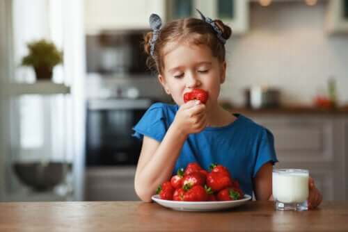 Bambina che mangia le fragola tra la frutta da mangiare in estate.