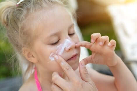 Mamma aiuta una bambina a spalmarsi la crema solare sul viso.