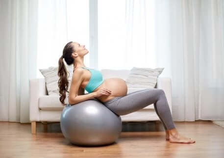 Donna incinta fa esercizi sulla palla fitness.