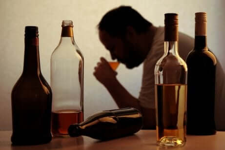 Alcolista beve alcolici con bottiglie vuote sul tavolo.