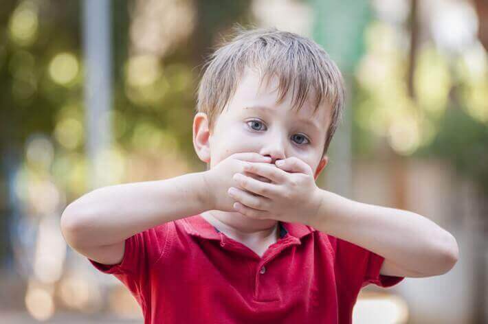 Bambino balbuziente con mani sulla bocca.