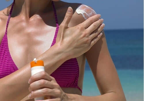 Donna applica la crema solare sulle spalle.