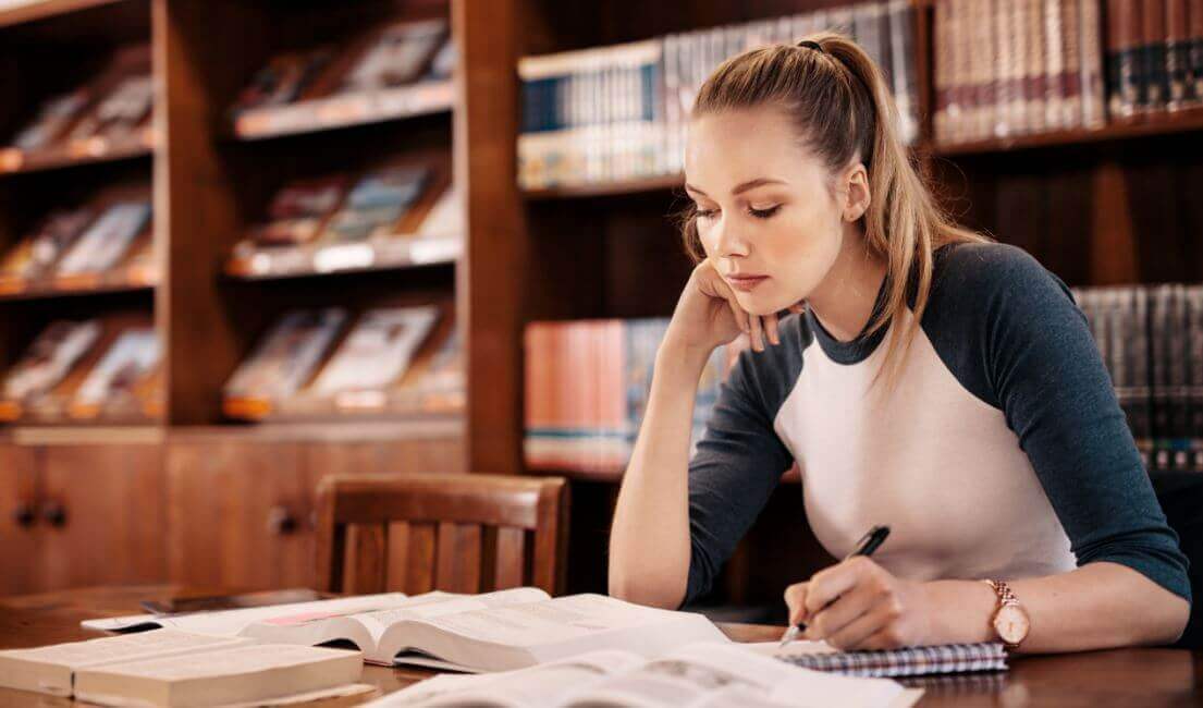 Ragazza giovane bionda studia in biblioteca.