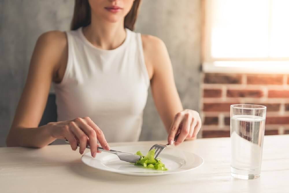 Ragazza magra davanti a un piatto di insalata.