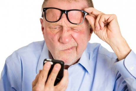 Uomo anziano solleva gli occhiali per leggere sul cellulare.